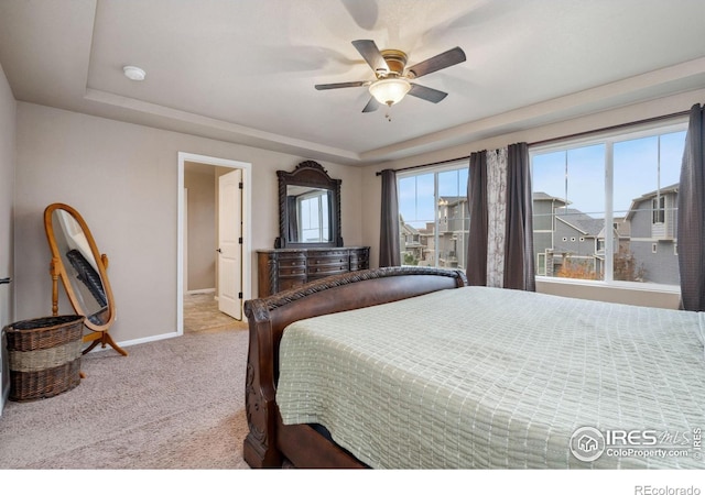 bedroom featuring a tray ceiling, light colored carpet, and ceiling fan