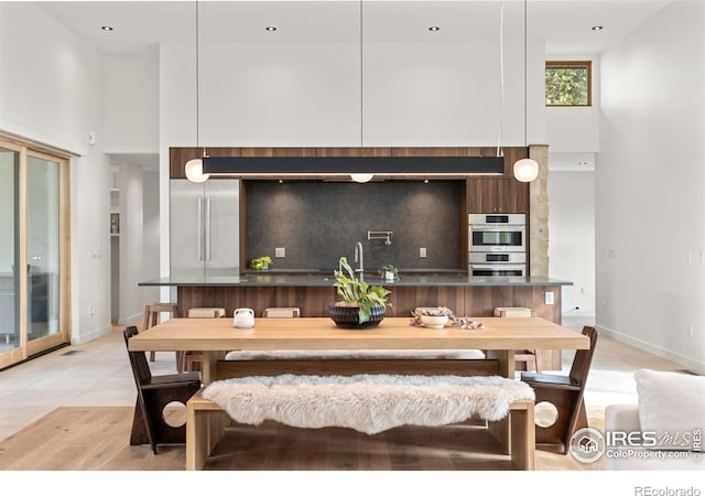 dining area featuring sink, a towering ceiling, and light wood-type flooring