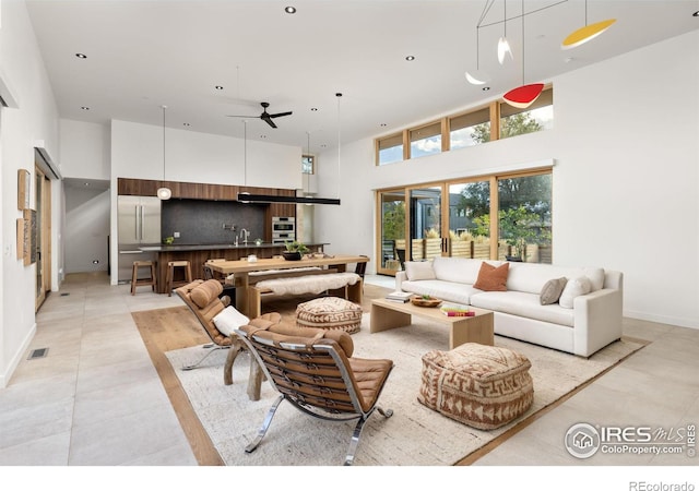 living area featuring ceiling fan, light tile patterned flooring, recessed lighting, visible vents, and a towering ceiling