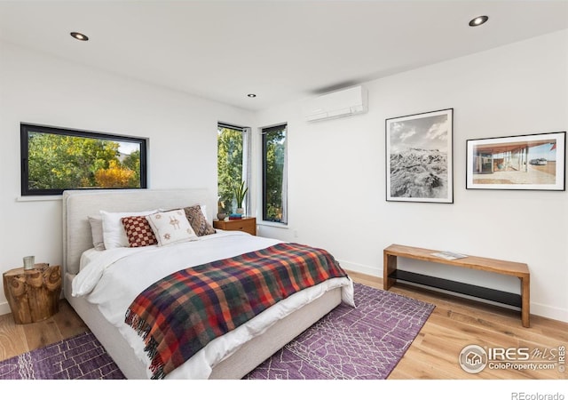 bedroom featuring recessed lighting, an AC wall unit, baseboards, and wood finished floors