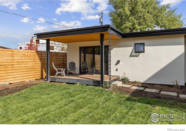 rear view of property with stucco siding, fence, a wooden deck, and a lawn