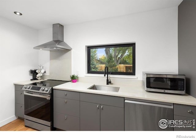 kitchen with wall chimney exhaust hood, stainless steel appliances, gray cabinetry, light wood-type flooring, and a sink