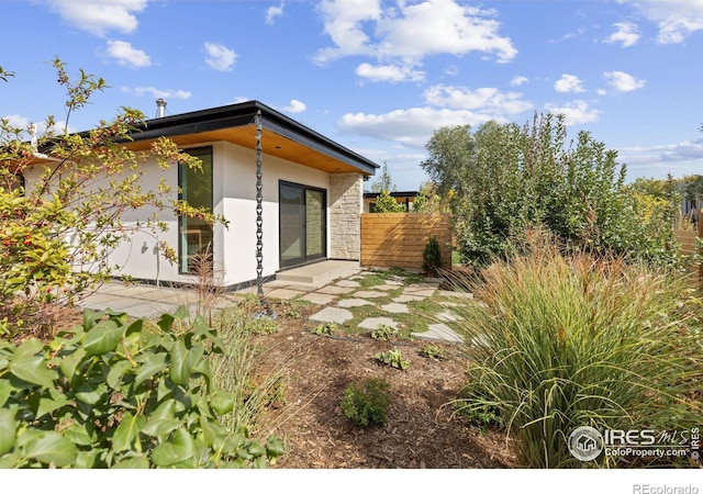 back of house featuring stone siding, fence, and stucco siding