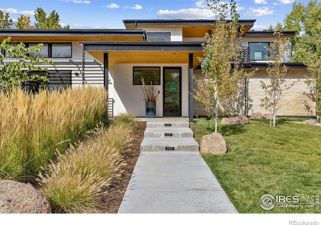 contemporary house featuring covered porch, a front yard, and stucco siding