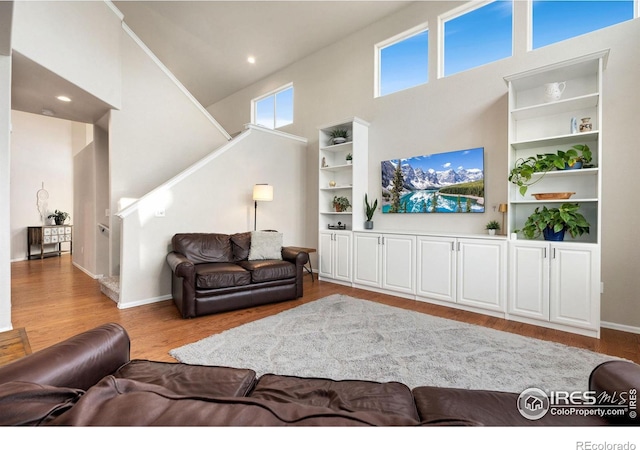 living room featuring wood-type flooring, built in features, and a high ceiling