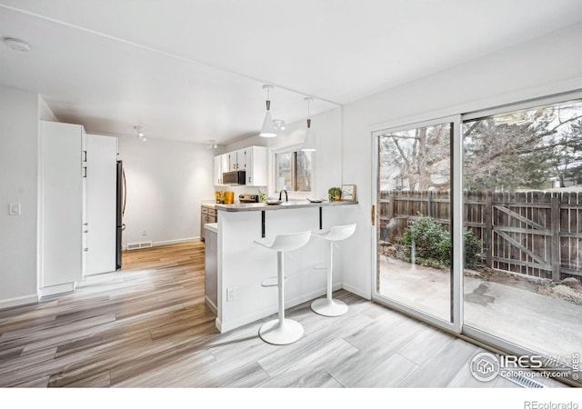 kitchen featuring appliances with stainless steel finishes, a kitchen breakfast bar, white cabinets, decorative light fixtures, and kitchen peninsula