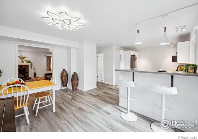 kitchen with pendant lighting, stainless steel refrigerator, a kitchen breakfast bar, white cabinets, and light wood-type flooring