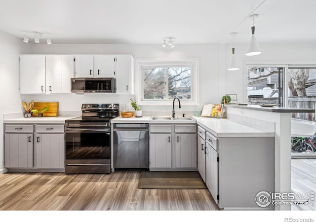 kitchen with appliances with stainless steel finishes, pendant lighting, sink, kitchen peninsula, and light wood-type flooring