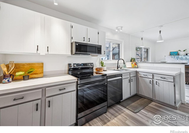 kitchen with sink, stainless steel appliances, light hardwood / wood-style floors, white cabinets, and kitchen peninsula