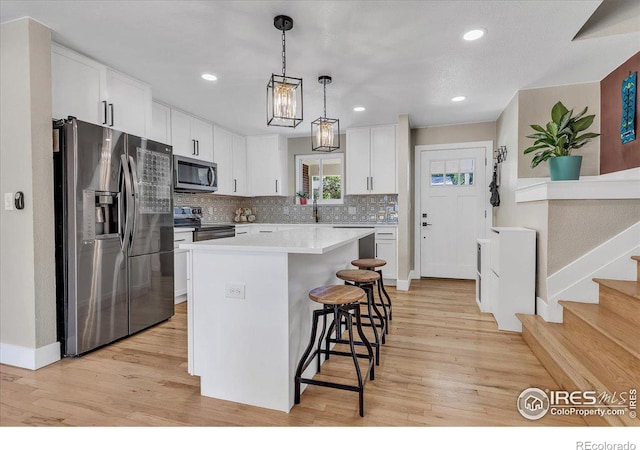 kitchen featuring pendant lighting, appliances with stainless steel finishes, a kitchen island, white cabinets, and a kitchen bar