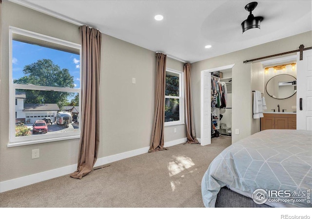 bedroom with ensuite bath, a barn door, a spacious closet, light colored carpet, and a closet