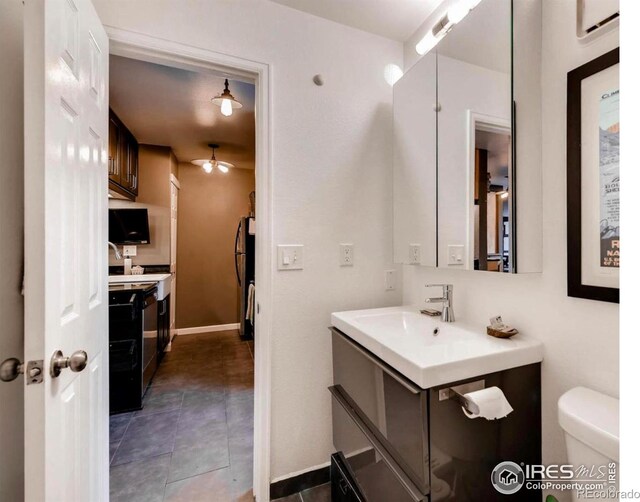 half bath with vanity, toilet, tile patterned flooring, ceiling fan, and baseboards