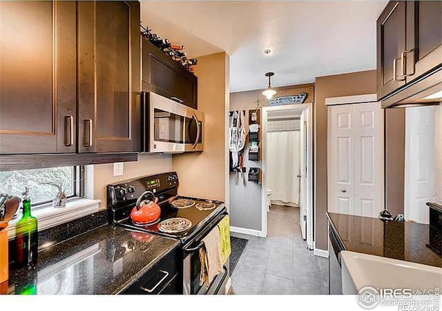 kitchen with range with electric cooktop, stainless steel microwave, dark brown cabinetry, light tile patterned flooring, and dark stone countertops
