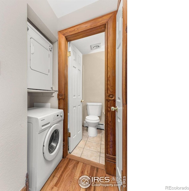 laundry area featuring light hardwood / wood-style flooring, a baseboard radiator, and stacked washer / dryer