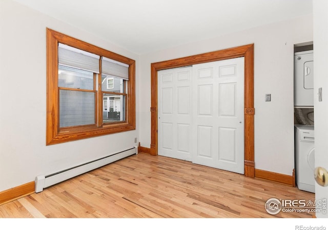 unfurnished bedroom with a baseboard heating unit, light hardwood / wood-style flooring, a closet, and stacked washing maching and dryer