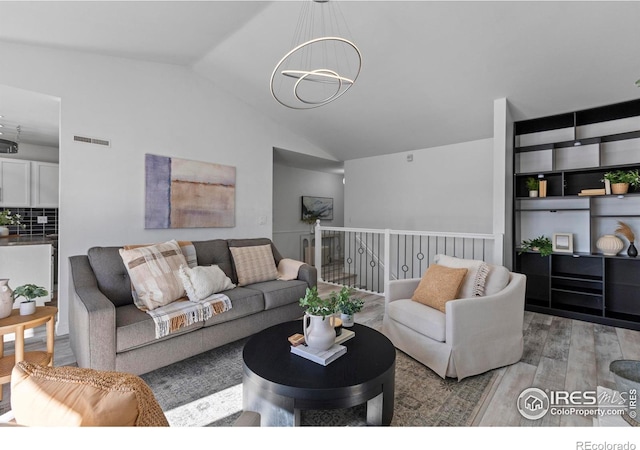 living room featuring lofted ceiling, light hardwood / wood-style floors, and an inviting chandelier