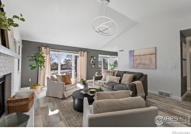 living room featuring a brick fireplace, a wealth of natural light, a notable chandelier, and light hardwood / wood-style flooring