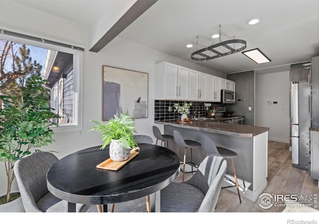 kitchen featuring appliances with stainless steel finishes, tasteful backsplash, white cabinets, kitchen peninsula, and light wood-type flooring