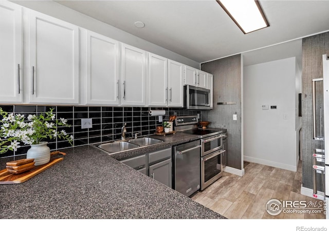 kitchen with appliances with stainless steel finishes, white cabinetry, sink, backsplash, and light hardwood / wood-style flooring