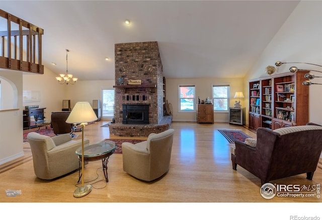 living room featuring an inviting chandelier, a fireplace, high vaulted ceiling, and light wood-type flooring