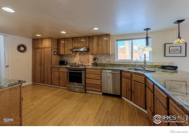 kitchen featuring stainless steel appliances, light hardwood / wood-style floors, sink, and hanging light fixtures