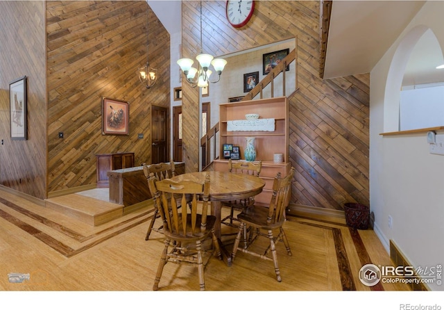 dining area featuring a towering ceiling, wood walls, and a notable chandelier