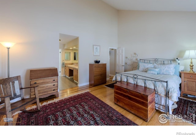 bedroom featuring ensuite bathroom, light hardwood / wood-style floors, and a high ceiling