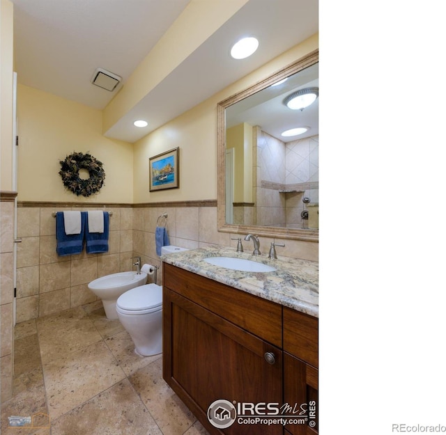 bathroom with a bidet, vanity, tile walls, and toilet