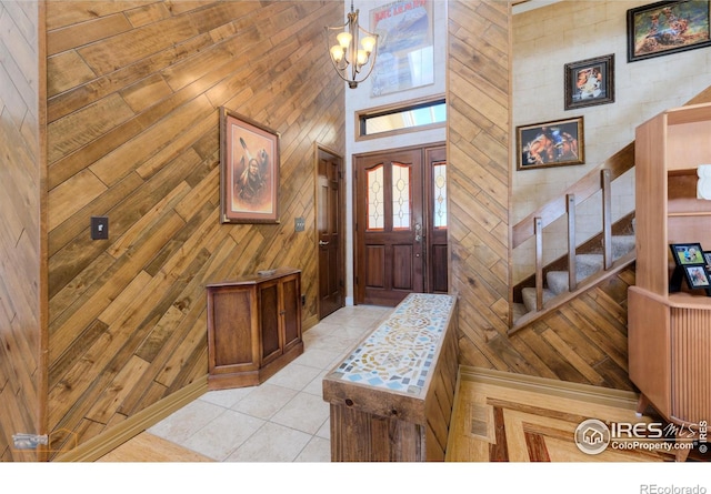 foyer with light tile patterned floors, a notable chandelier, and wooden walls