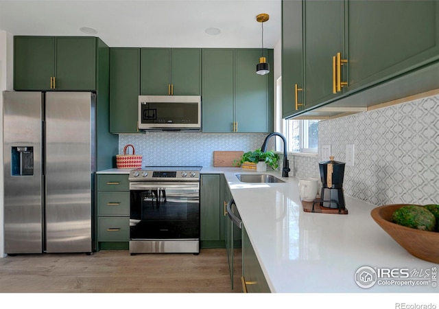 kitchen featuring sink, green cabinets, pendant lighting, stainless steel appliances, and backsplash