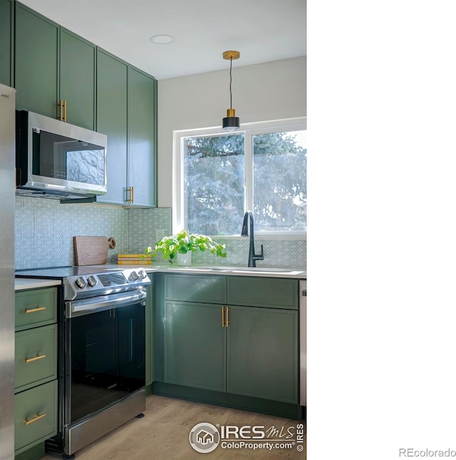 kitchen featuring sink, backsplash, green cabinets, light hardwood / wood-style floors, and stainless steel appliances