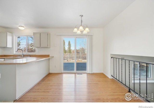 kitchen with white cabinetry, hanging light fixtures, light hardwood / wood-style flooring, and sink