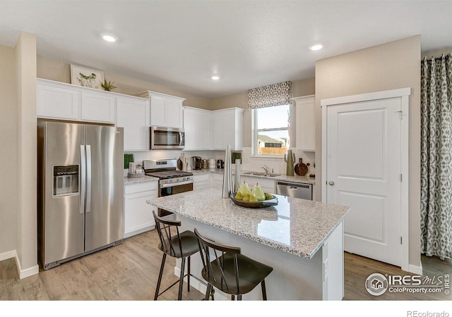 kitchen featuring light hardwood / wood-style flooring, appliances with stainless steel finishes, white cabinetry, light stone countertops, and a kitchen island