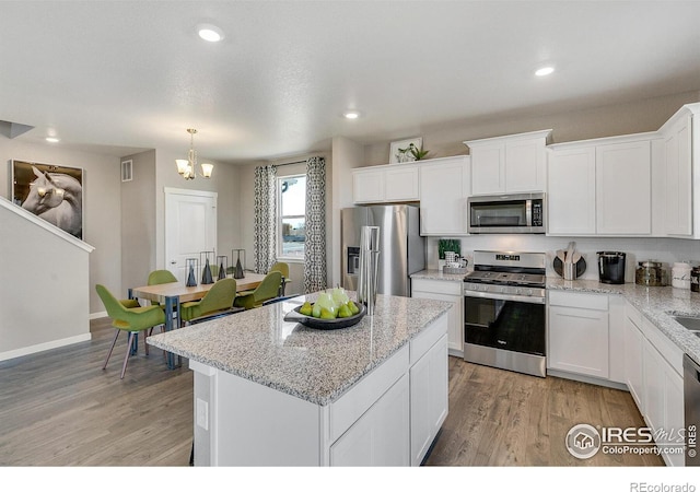 kitchen featuring a kitchen island, white cabinetry, hanging light fixtures, stainless steel appliances, and light wood-type flooring