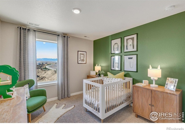 bedroom featuring a nursery area, light carpet, and a textured ceiling