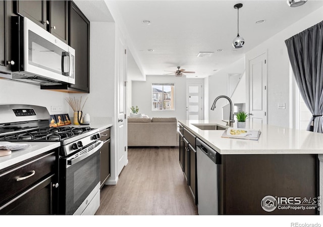 kitchen featuring a center island with sink, appliances with stainless steel finishes, light wood-style floors, open floor plan, and a sink