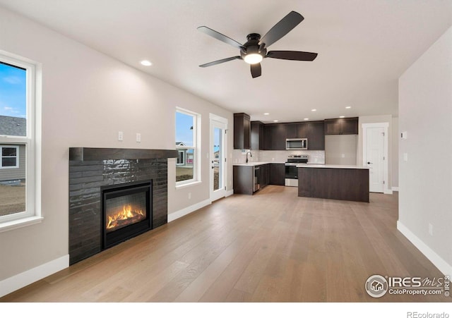 7172 Feather Reed Dr, Wellington, CO 80549 - kitchen with light countertops, ceiling fan, dark brown cabinets, a stone fireplace, and appliances with stainless steel finishes