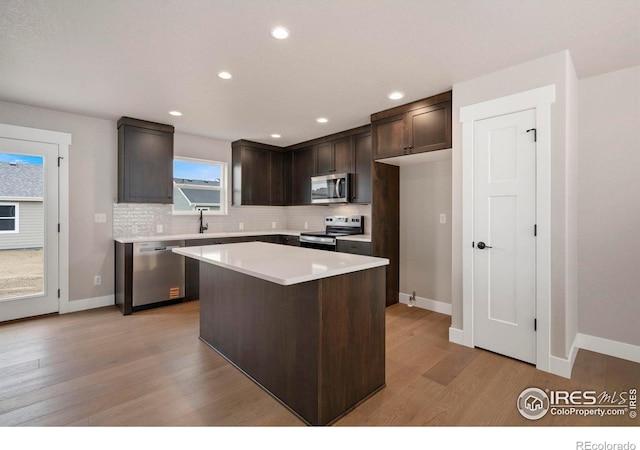7172 Feather Reed Dr, Wellington, CO 80549 - kitchen with decorative backsplash, light wood-style flooring, stainless steel appliances, dark brown cabinets, and a center island