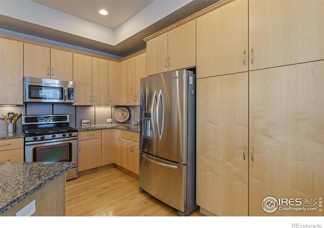 kitchen featuring stainless steel appliances, light brown cabinetry, and dark stone counters