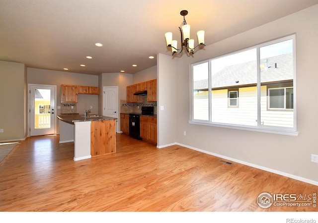 kitchen with a chandelier, light hardwood / wood-style flooring, an island with sink, black range with electric cooktop, and pendant lighting