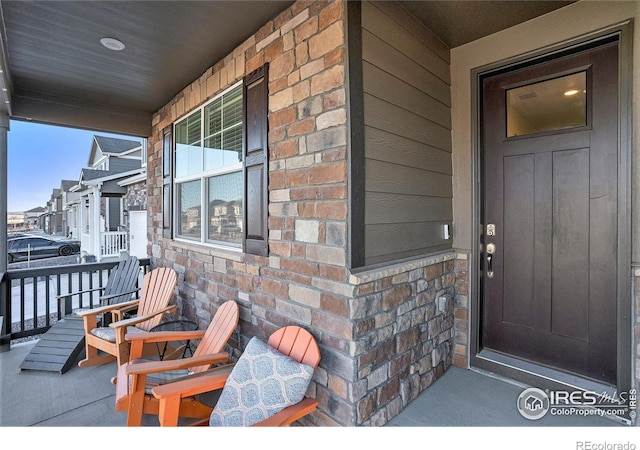 doorway to property featuring a porch, brick siding, and stone siding