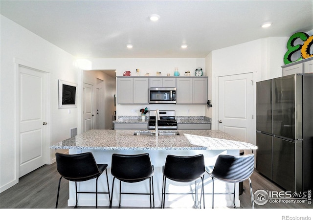 kitchen with a kitchen bar, dark wood-type flooring, gray cabinets, a sink, and appliances with stainless steel finishes