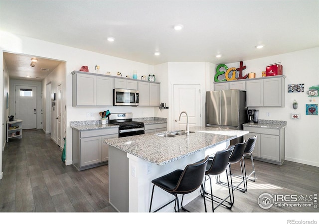 kitchen with an island with sink, a sink, a kitchen breakfast bar, wood finished floors, and stainless steel appliances