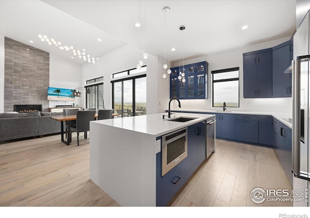 kitchen featuring blue cabinets, light wood-type flooring, modern cabinets, a center island with sink, and a sink