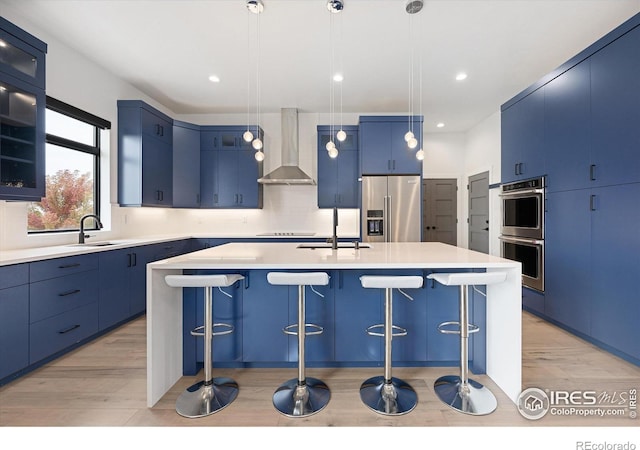 kitchen featuring blue cabinets, a sink, stainless steel appliances, a breakfast bar area, and wall chimney range hood