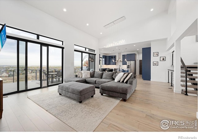 living area featuring stairs, recessed lighting, light wood-type flooring, and a towering ceiling