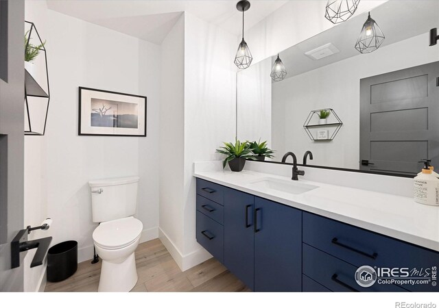 half bathroom featuring vanity, toilet, wood finished floors, and baseboards