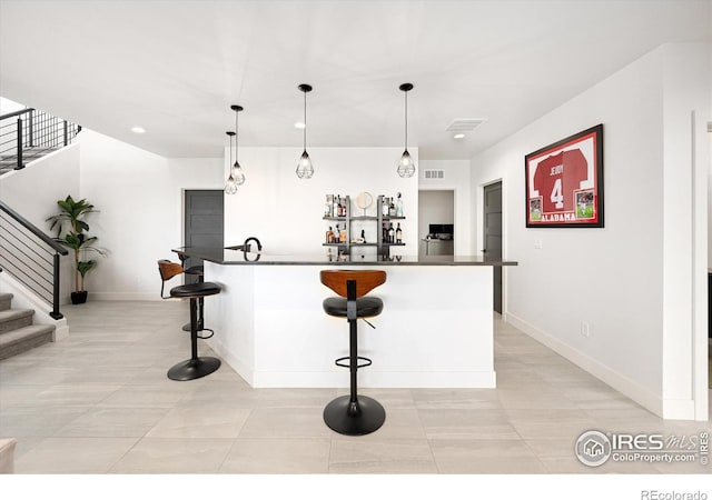 kitchen featuring dark countertops, visible vents, baseboards, pendant lighting, and a kitchen bar