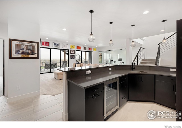 kitchen featuring beverage cooler, a sink, dark countertops, dark cabinetry, and recessed lighting