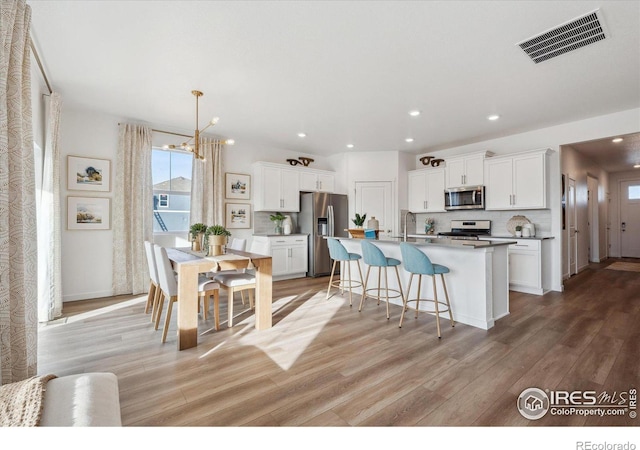 kitchen featuring light hardwood / wood-style flooring, appliances with stainless steel finishes, white cabinetry, tasteful backsplash, and an island with sink